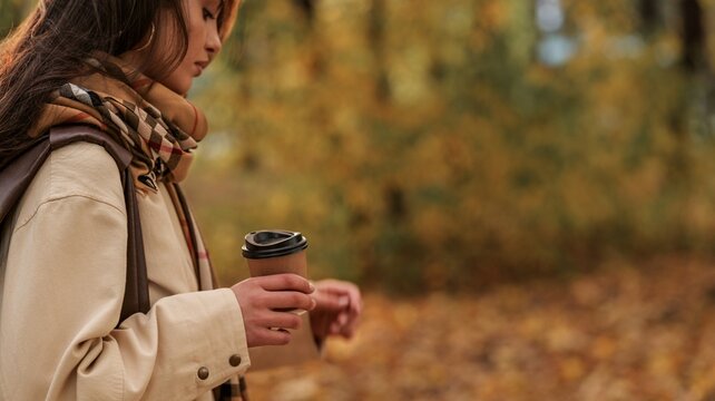 Woman holding a takeaway coffee cup amid warm autumn foliage in a quiet park setting