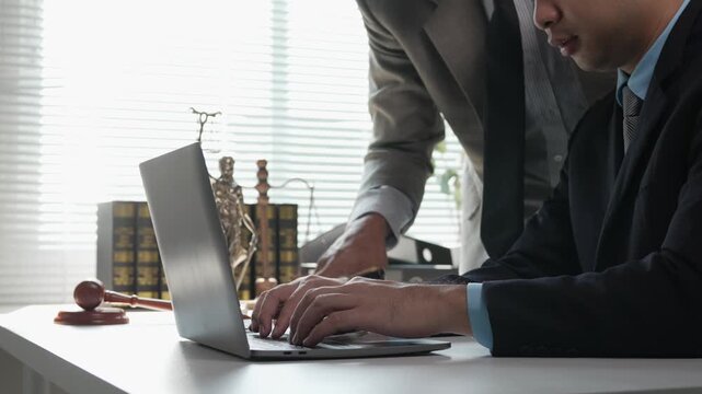 Male lawyer consulting with a colleague in a law office while discussing a legal case and pointing at a laptop screen