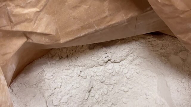 White powder stored in multiple bags, representing a batch of suspected cocaine. Close view into open brown kraft paper bag containing fine white powder. Illegal drug
