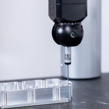 Coordinate measuring machine probe with ruby tip inspecting a precision machined aluminium component on a granite table, quality control