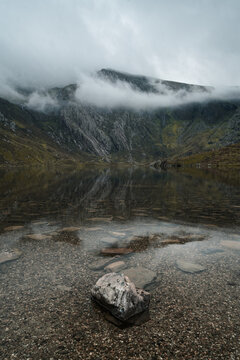 Clear mountain lake with submerged rock foreground and mist covered ridge in Eryri National Park