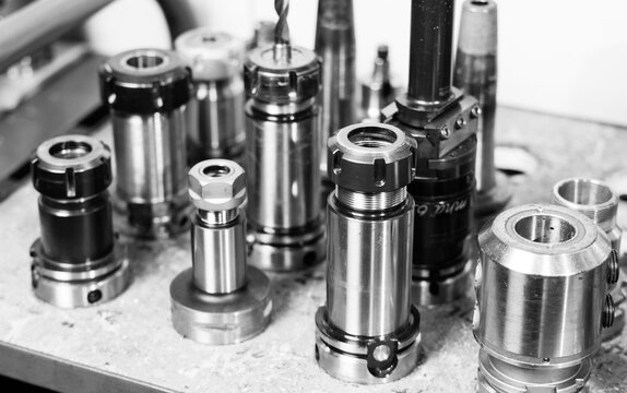 Black and white close-up of CNC collet chucks and tool holders arranged on a workshop bench, precision machining tooling