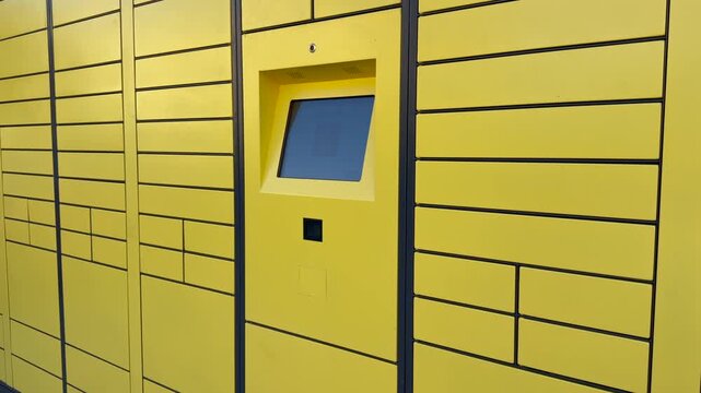 Yellow parcel lockers form automated delivery system with touchscreen access kiosk for convenient package pickup. Modular compartments offer practical logistics. Modern locker station for pickup