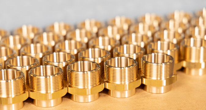 Rows of precision machined brass threaded hex fittings on a cardboard surface, close-up, CNC manufacturing