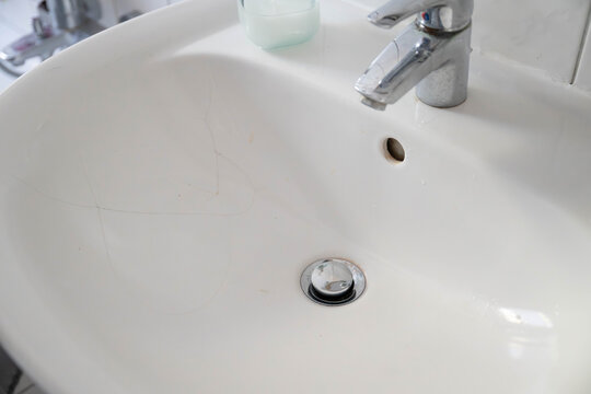 Bathroom sink and faucet showing signs of wear, with visible limescale deposits on the fixture. Damaged bathroom surfaces, hard water buildup, and the need for cleaning, maintenance, or plumbing renov