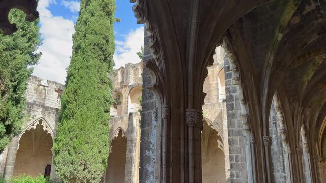 Kyrenia, Cyprus - October 3, 2026 Bellapais Abbey courtyard framed by Gothic stone arches and ribbed vaulting. Camera glides along cloister beside tall cypress, revealing sunlit garden and historic