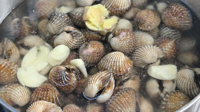 Fresh clams are boiled with garlic and aromatic herbs in a pot. This cooking process enhances rich flavors while removing unwanted fishy odors.