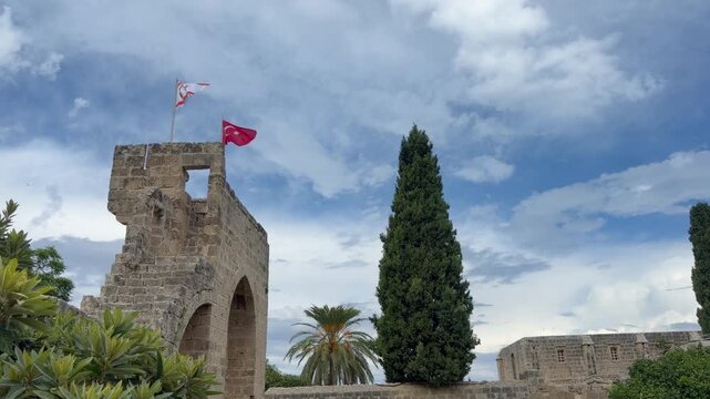 Kyrenia, Cyprus - October 3, 2026 Bellapais Abbey rises beneath cloudy blue sky, its Gothic stone tower framed by cypress trees. Pointed arches and historic masonry define this Cypriot landmark.