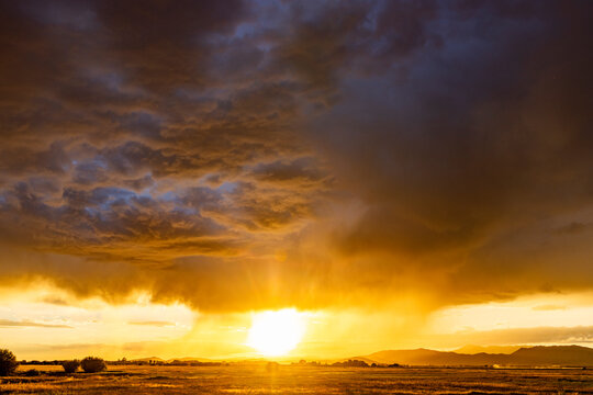 Heavy rain clouds and sun setting above landscape
