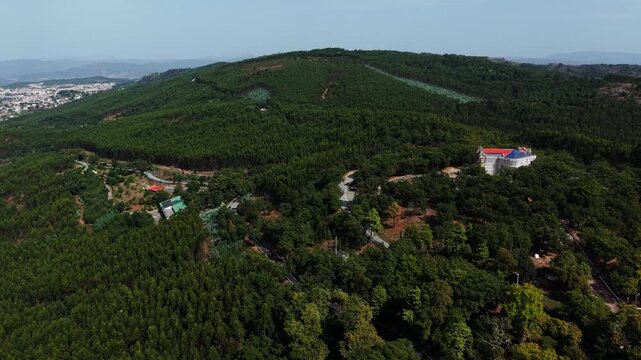 Drone flight over dense forest on the Falperra hills toward Sameiro, with a hotel building among trees and Braga suburbs at one edge.