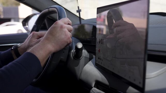 Close-up inside a modern vehicle showing a driver gripping the steering wheel next to a large digital navigation touchscreen display