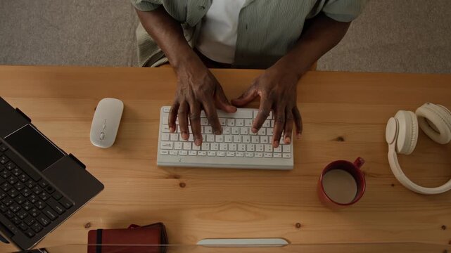 Hands of African American young adult man typing on keyboard and using mouse in high angle view. Clip suitable for remote work, programming, IT development, and business workflow campaigns