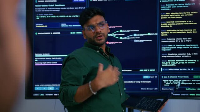 Male DevOps Engineer Holding Digital Tablet and Explaining Software Deployment Architecture and Discussing Development Operations Strategy with Colleagues Reviewing Programming Code on Large Screen.