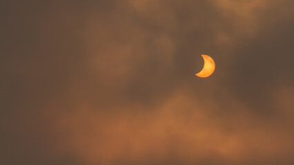 Partial solar eclipse glowing through cloudy sunset sky © David