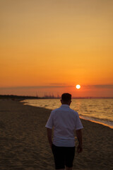 Rear view of a man walking on a sandy beach at sunset, enjoying the peaceful atmosphere of the sea, perfect for travel or lifestyle themes © Olga Yashnikova