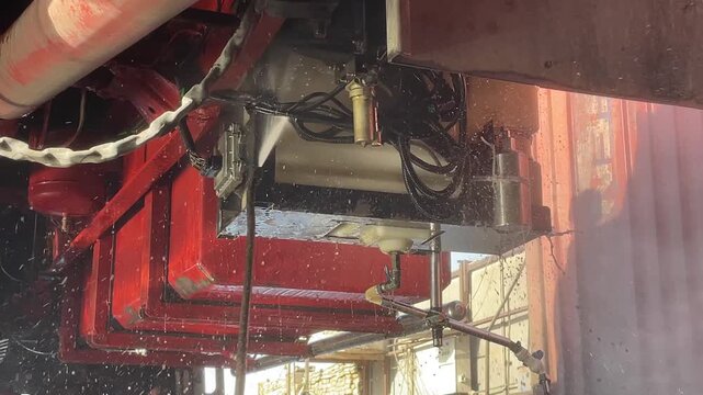 Truck chassis rails frame a network of hoses and metal components under the cargo bed, with water mist visible during underside cleaning, highlighting vehicle care as part of vehicle upkeep.