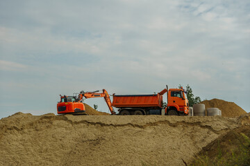 Orange excavator and dump truck on a sandy construction site. Heavy industrial machinery performing earthmoving tasks for infrastructure development © Olga Yashnikova