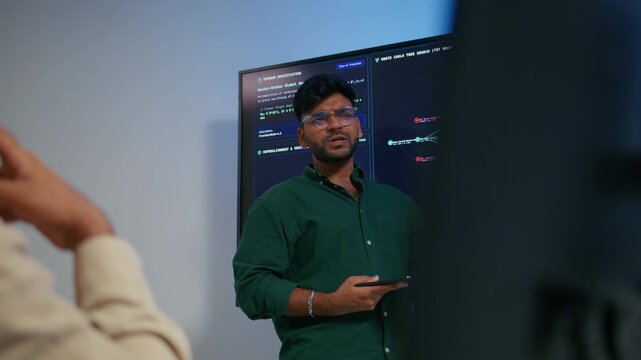 Male DevOps Engineer Holding Digital Tablet and Explaining Software Deployment Architecture and Discussing Development Operations Strategy with Colleagues Reviewing Programming Code on Large Screen.