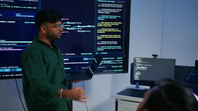 Male DevOps Engineer Holding Digital Tablet and Explaining Software Deployment Architecture and Discussing Development Operations Strategy with Colleagues Reviewing Programming Code on Large Screen.