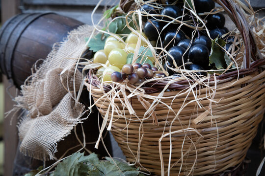 Rustic basket filled with dark green and red grapes beside burlap fabric and wooden barrel creating harvest still life with natural textures and soft market style charm in close view detail around