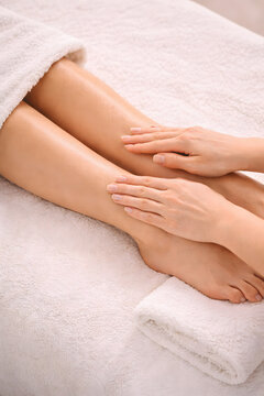 Lower leg lymphatic massage is performed with gentle hand strokes around the ankle and shin while the woman's legs rest on folded towels.
