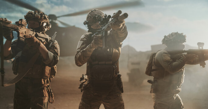 Trio of Commandos in Multicam Uniforms, Ballistic Helmets and Night Vision Mounts Raise Assault Rifles in a 360-degree Cordon, Scanning for Threats Through Dust Kicked up by a Helicopter in Desert.