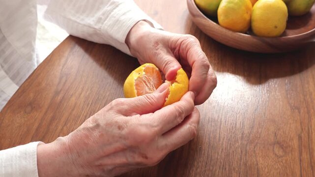 木製テーブルでみかんを食べる高齢女性の手元のアップ