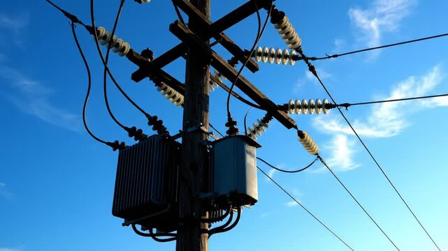 Low-angle shot of a utility pole with transformers and power lines against a clear blue sky