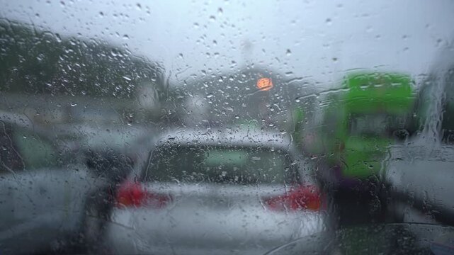 Raindrops cover a car windshield as vehicles wait in slow traffic on a grey rainy day, blurred background, New Zealand