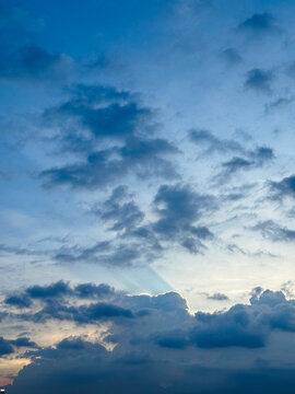 Dramatic blue sky with clouds and sunlight glowing behind cloud edge at dusk