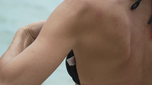 Adjusting red bikini straps by woman at coastal shoreline on sunny vacation. Close-up static shot.
