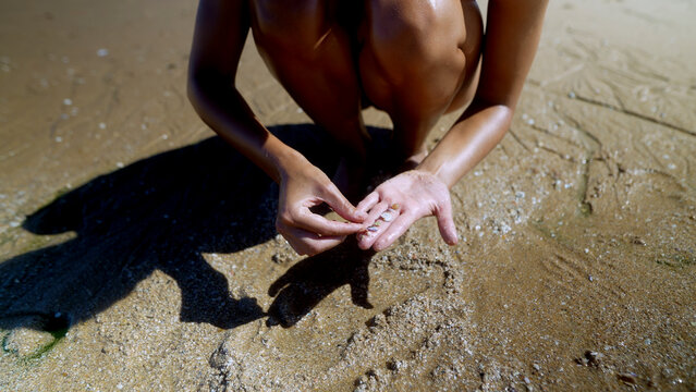 Woman examining wet sand in her palm at the shoreline