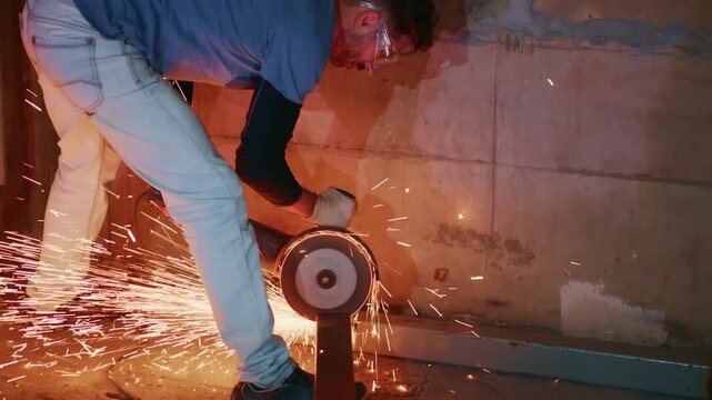 Worker cuts metal with grinder, sparks fly. Safety goggles shield eyes from flying debris. Dust and heat surround the cutting zone. Industrial scene shows skilled labor and mechanical precision