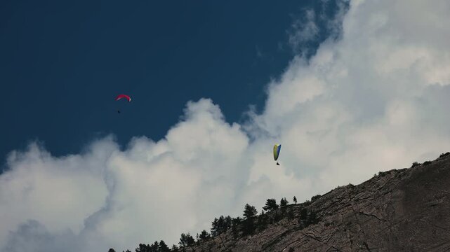 paragliders soaring high above scenic mountain cliffs and white clouds under a deep blue sky.