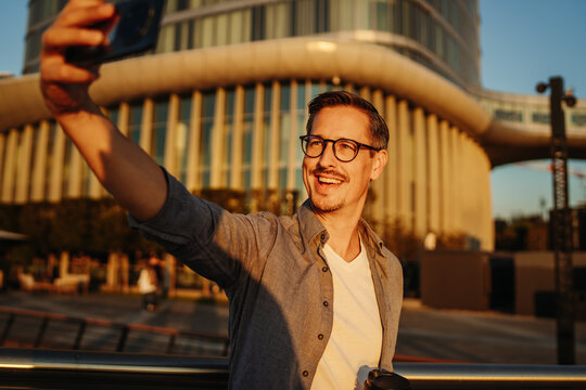 Smiling man taking selfie in city at golden hour