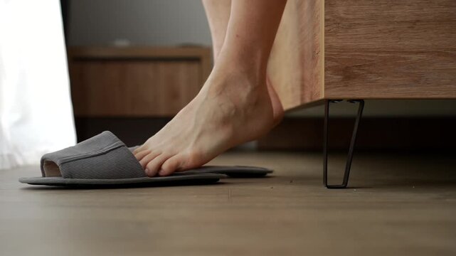 Grey house slippers on the floor.
A person gets out of bed in the morning and puts on soft slippers.