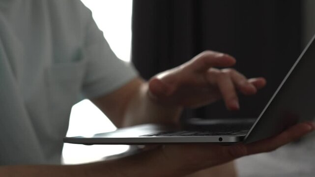 A man in a light T-shirt works on a laptop while sitting comfortably in a bright room. The scene represents remote work, freelancing, online business, and the everyday lifestyle of IT professionals