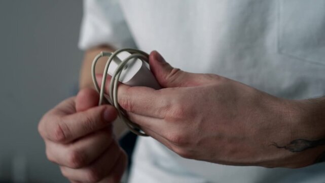 Close-up of a man holding a white phone charger and a charging cable in his hands. The video shows mobile phone accessories used for charging electronic devices in everyday life.