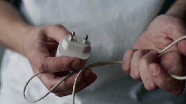 Close-up of a man holding a white phone charger and a charging cable in his hands. The video shows mobile phone accessories used for charging electronic devices in everyday life.