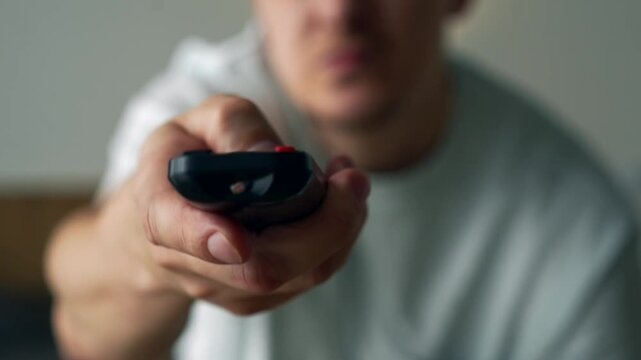 Frustrated Young Man Trying to Change TV Channels with a Malfunctioning Remote Control