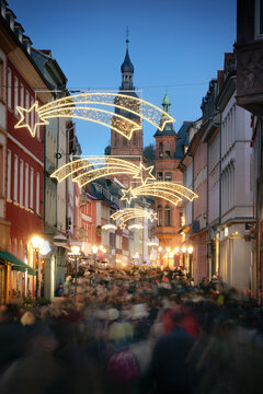 Loads of people with motion blur rushing and shopping on the historic German city of Heidelberg at Christmas. With holiday decoration and buildings leading to a church.