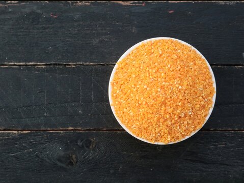 Top view of raw yellow corn grits in a white bowl placed on a rustic dark wooden table with copy space. Perfect background for healthy food, organic grain, and cooking recipes