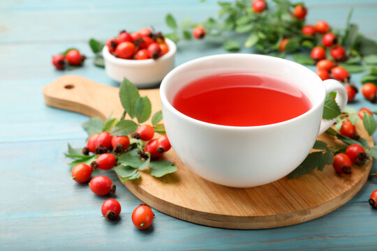 Aromatic rosehip tea in cup, berries and green leaves on light blue wooden table, closeup. Space for text