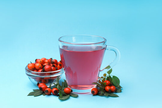 Rosehip tea in cup and berries with leaves on light blue background