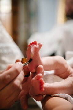 Priest anointing baby foot with sacred chrism oil using brush during orthodox baptism sacrament closeup.