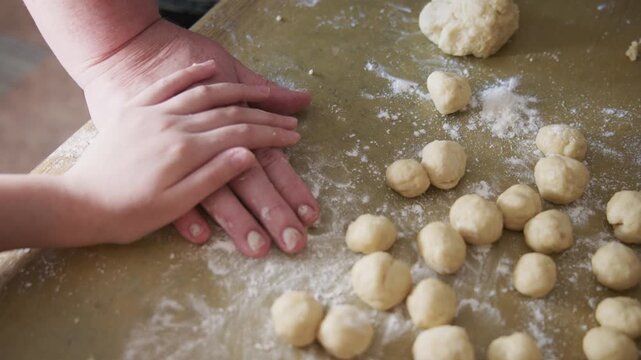 Hands shape dough on floury surface. Kneading motion suggests care and attention. Warm kitchen scene invites cozy cooking moments. Ideal for food, family, or home baking projects