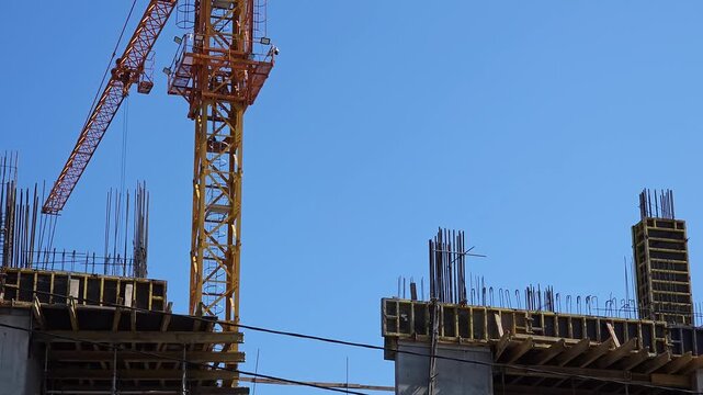 Tower crane operating beside an unfinished reinforced concrete structure with exposed rebar and formwork, illustrating large scale urban construction, engineering, real estate development and infrastr