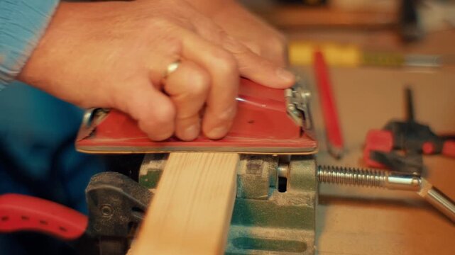 Slow motion close-up of hands using a red sanding block to smooth a wooden plank clamped in a vise. Authentic DIY woodworking footage for craft, carpentry and maker projects
