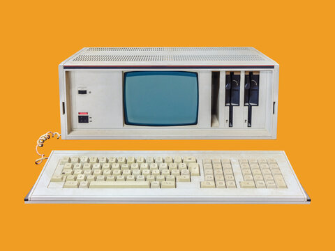 Vintage eighties portable desktop computer with crt display and floppy drives on an orange background