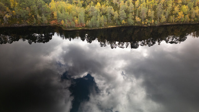 Aerial view of Loch Beinn a' Mheadhoin in Glen Affric featuring calm water reflecting the surrounding autumn forest and dramatic clouds in the sky in Beauly, Scotland, United Kingdom.